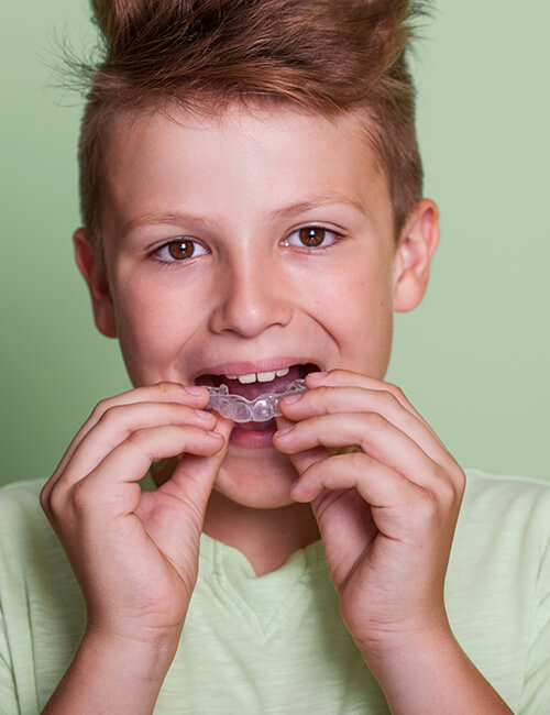 A boy holding a mouthguard near his teeth on a green background