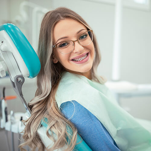 A blonde girl with glasses smiling while sitting on dentist chair