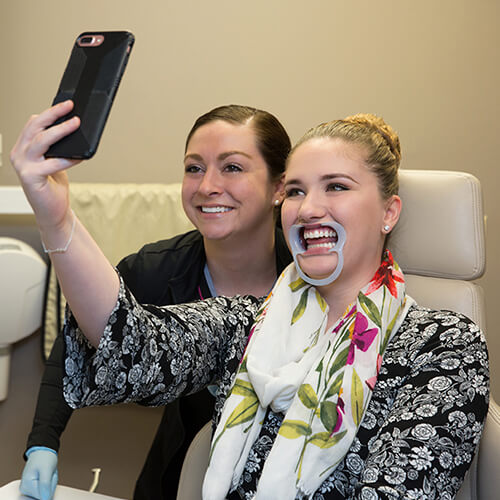 A woman patient smiling next to dental staff taking a selfie