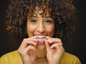 Curly-haired woman placing a clear aligner in her mouth